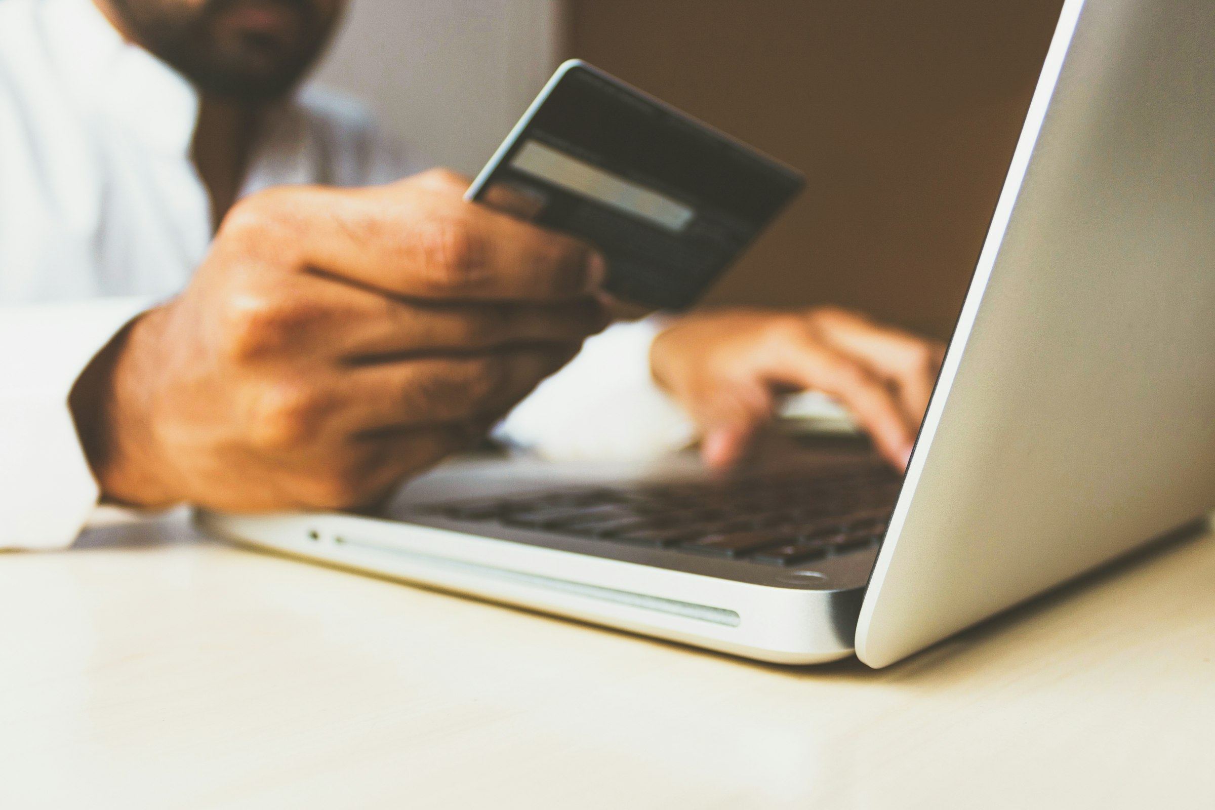 A person holds a bank card while they type on a laptop