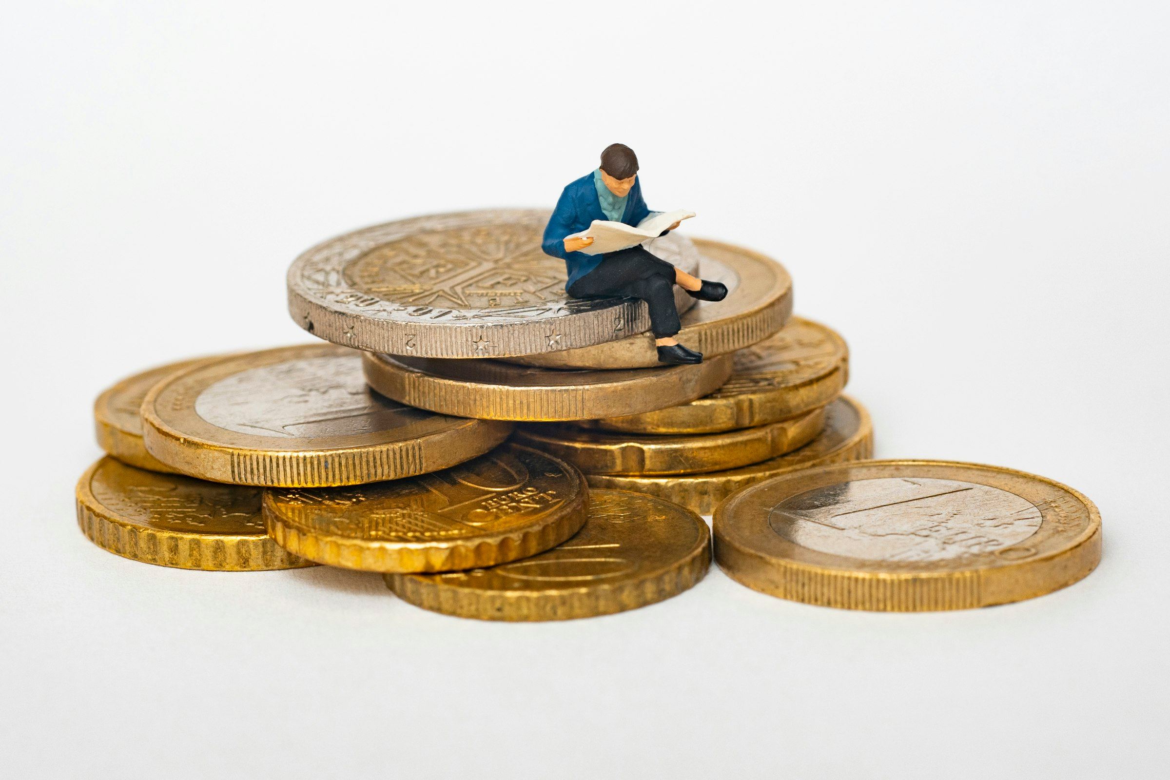 A tiny figure reads a book on top of a stack of euro coins