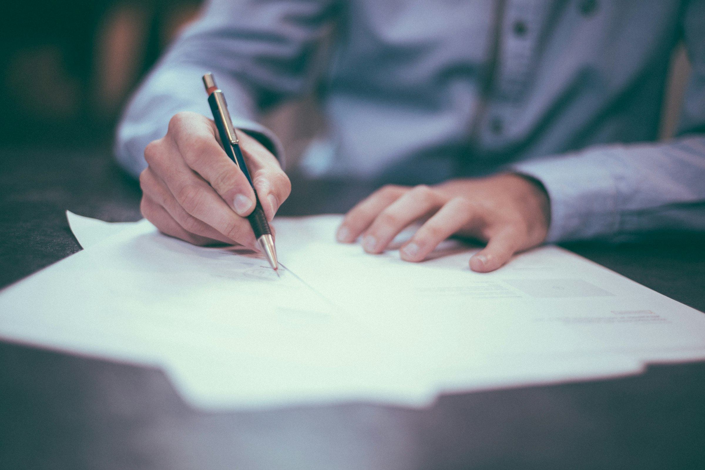 A person signs a printed document with a pen